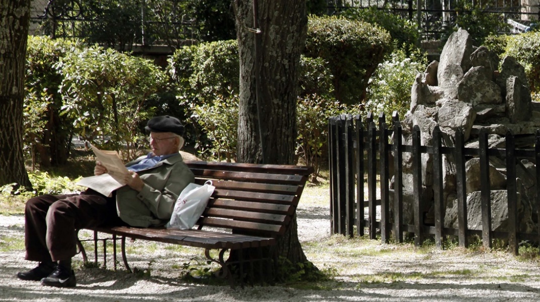 Συνταξιούχος διαβάζει την εφημερίδα του καθισμένος σε παγκάκι