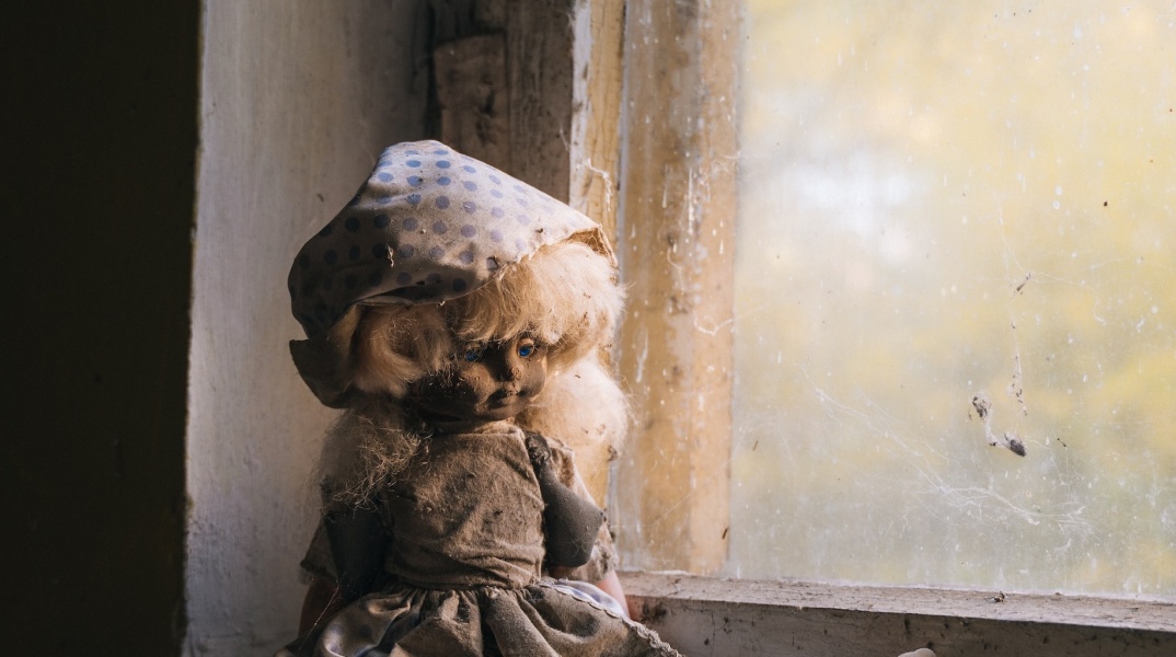 Λερωμένη και ταλαιπωρημένη κούκλα σε σκονισμένο παράθυρο