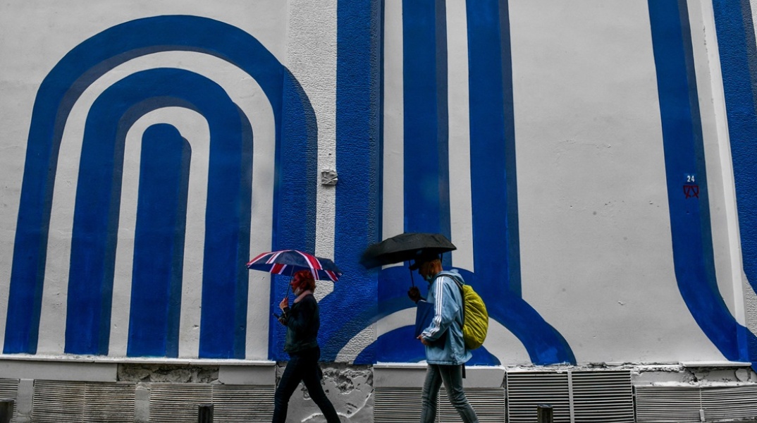 Πολίτες με ομπρέλα προστατεύονται από τη βροχόπτωση σε δρόμο της Αθήνας