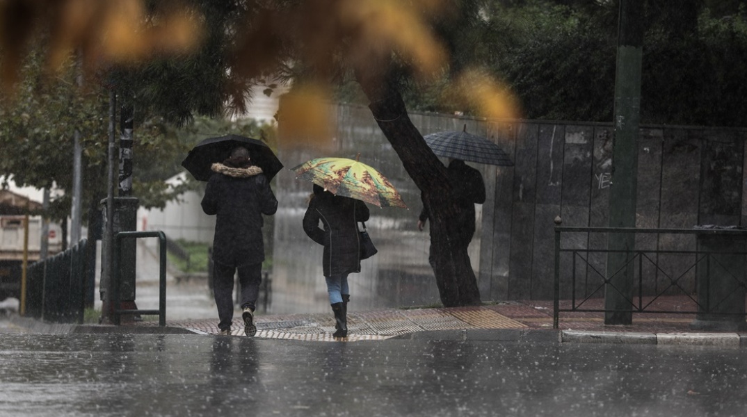 Πολίτες με ομπρέλα περπατούν υπό καταρρακτώδη βροχή