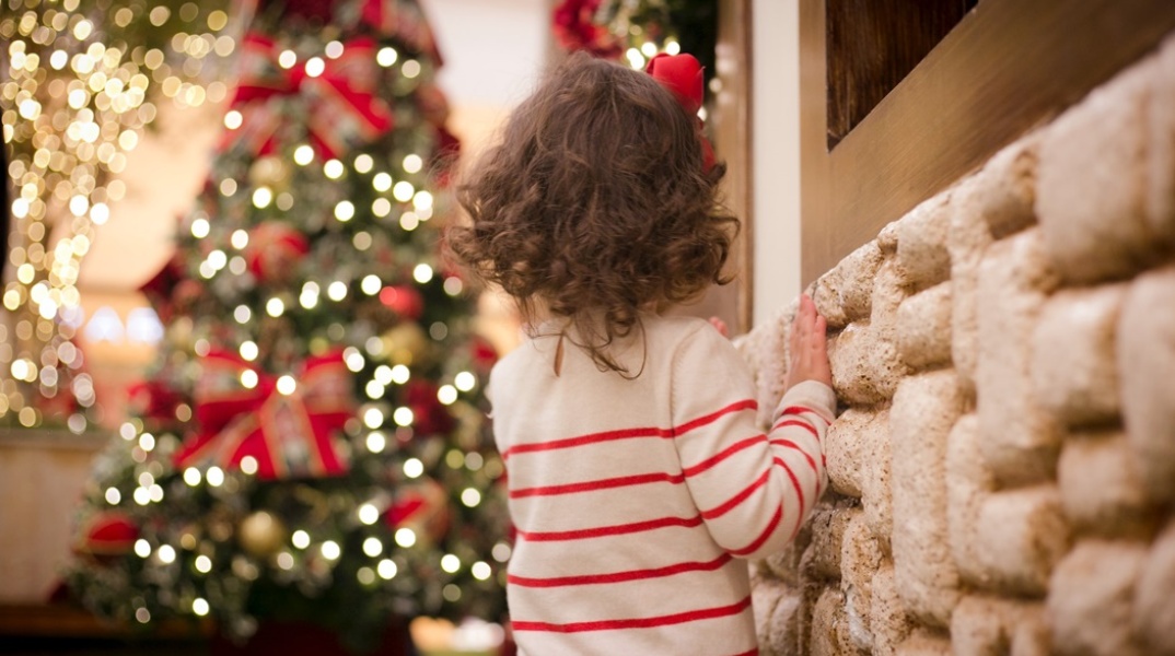 κοριτσάκι γυρισμένο σπίτι στην κάμερα με φόντο χριστουγεννιάτικο δέντρο