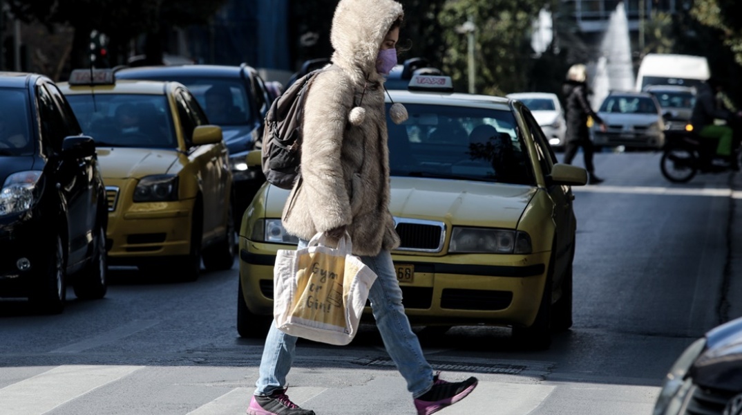Γυναίκα με ζεστό παλτό διασχίζει δρόμο στο κέντρο της Αθήνας