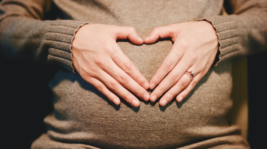 Έγκυος σχηματίζει στα χέρια της καρδιά μπροστά από τη φουσκωμένη της κοιλιά  