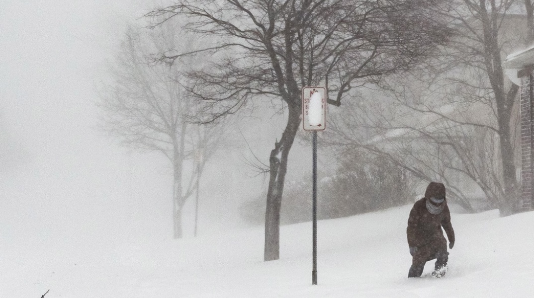 Γυναίκα περπατά με δυσκολία σε δρόμο που έχει καλυφθεί από αρκετούς πόντους χιονιού στις ΗΠΑ
