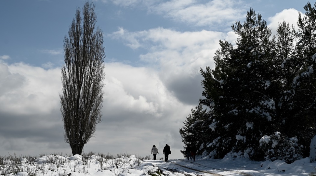 Πολίτες περπατούν σε χιονισμένο τοπίο