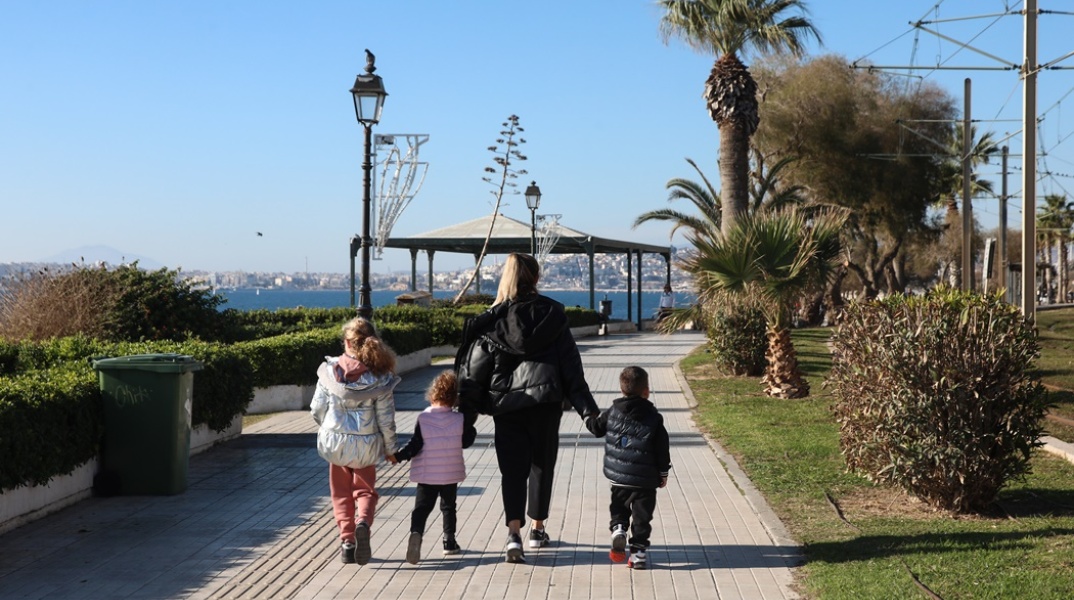 Μητέρα με τα τρία της παιδιά απολαμβάνουν τον καλό καιρό και τον ήλιο περπατώντας δίπλα στη θάλασσα