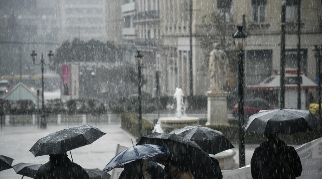 Πολίτες με ομπρέλα περπατούν υπό καταρρακτώδη βροχή στο κέντρο της Αθήνας