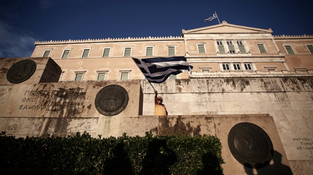 Άνδρας κυματίζει την ελληνική σημαία έξω από τη Βουλή των Ελλήνων