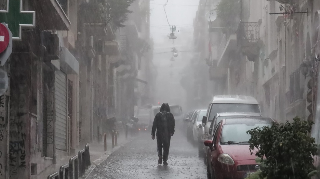 Άτομο κάτω από ισχυρή καταιγίδα σε δρόμο της Αθήνας - Υπό καταρρακτώδη βροχή στον δρόμο