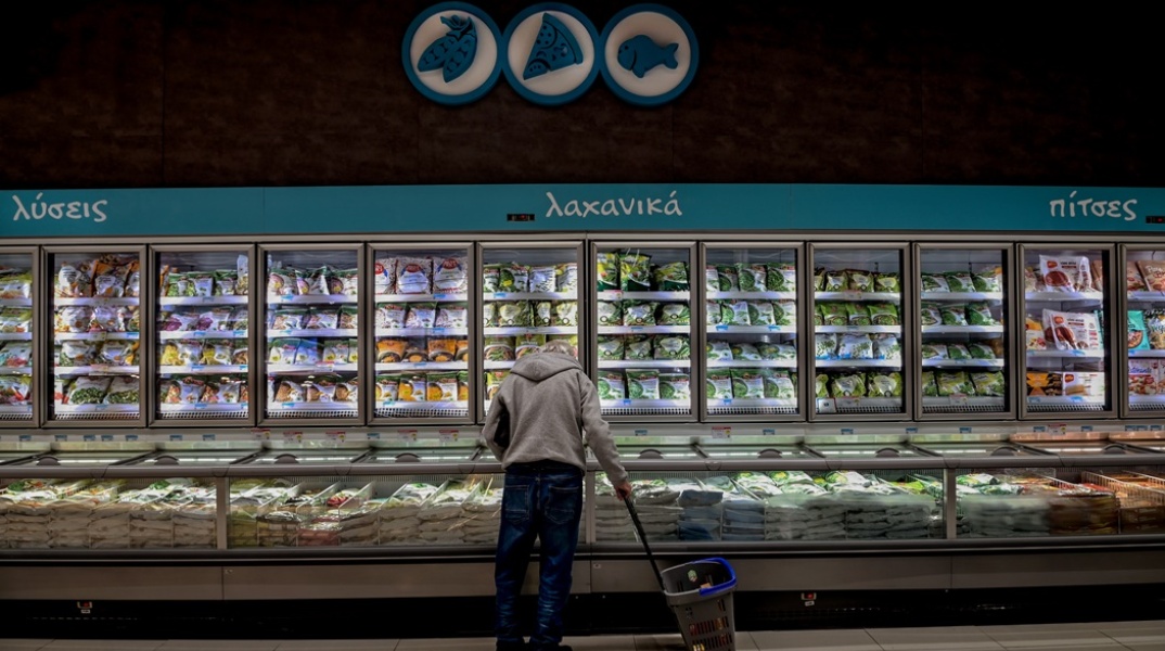 Πολίτες σε σούπερ μάρκετ κοιτά σε καλάθι με καταψυγμένα προϊόντα κρατώντας στο δεξί του χέρι το καλάθι
