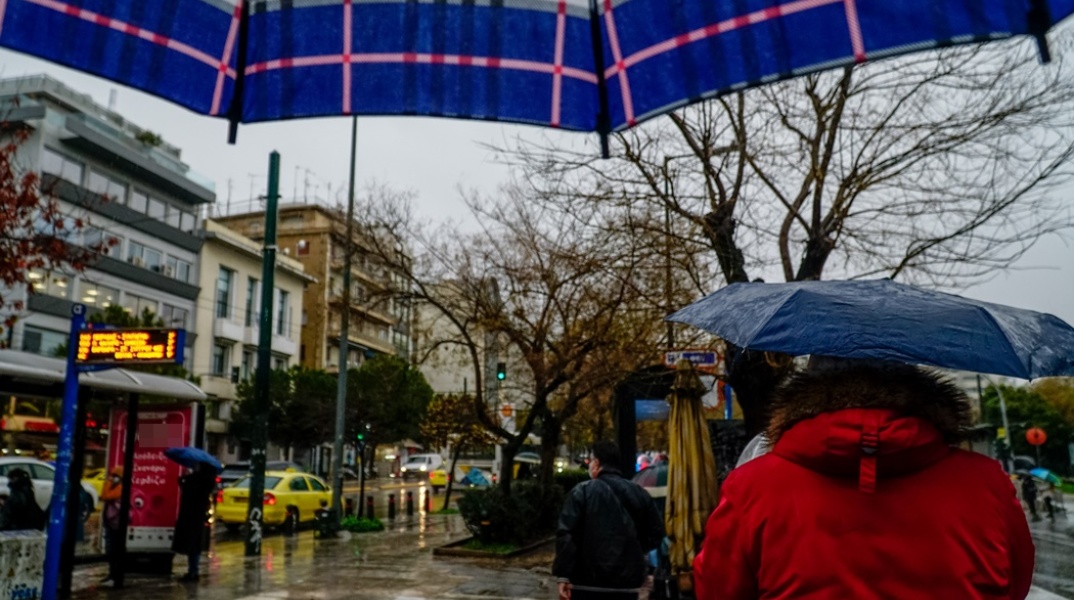 Πολίτες με ομπρέλα προστατεύονται από τη βροχή στο κέντρο της Αθήνας