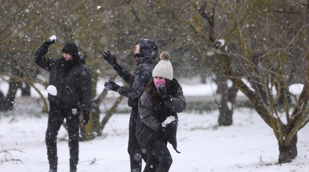 Νεαρά άτομα παίζουνε με το χιόνι, φορώντας ζεστά ρούχα