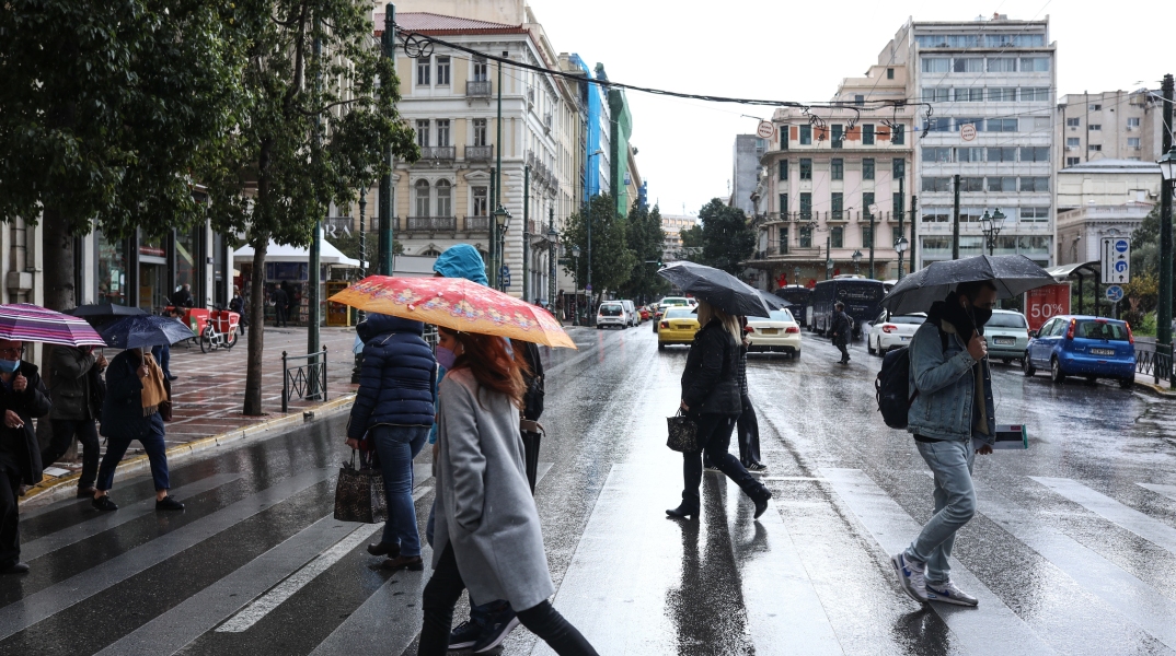 Πολίτες με ομπρέλα σε μία βροχερή μέρα στην καρδιά της Αθήνας