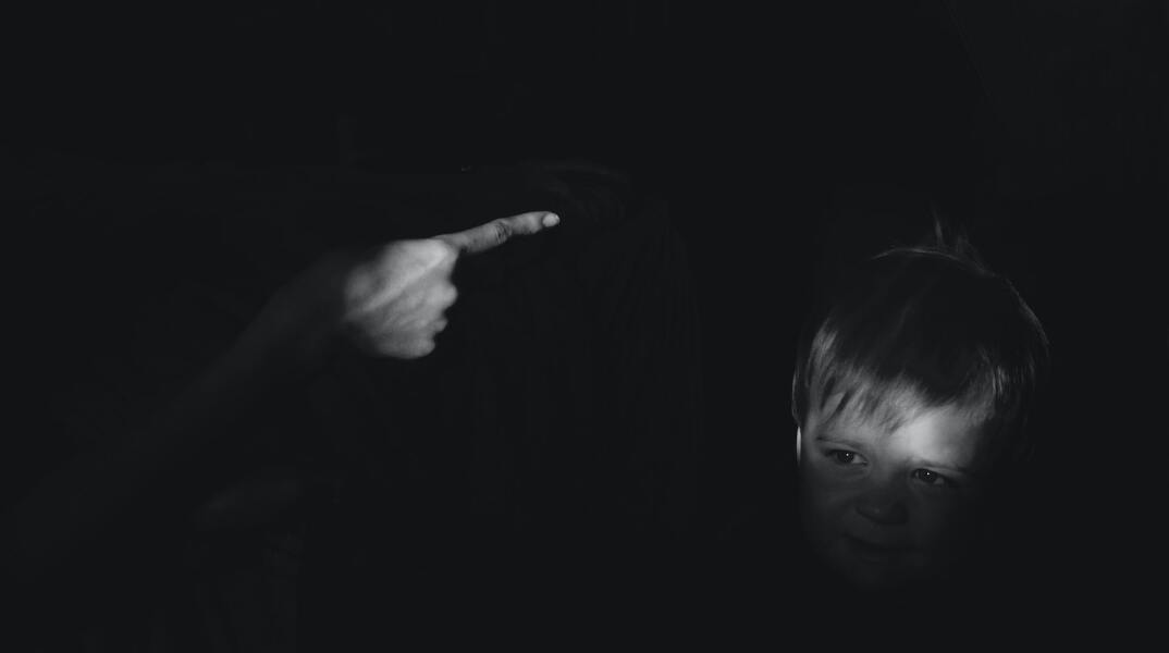 Γυναίκα τείνει το χέρι κατά παιδιού σε σκοτεινό δωμάτιο - Εικόνα που παραπέμπει σε κακοποιητική συμπεριφορά