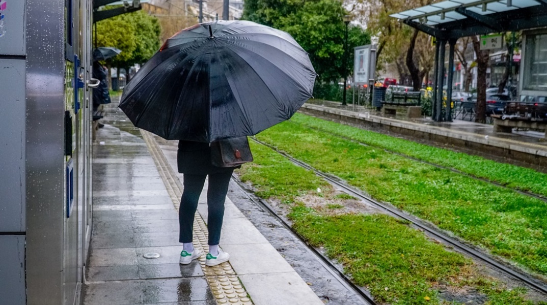Γυναίκα με ομπρέλα εν ώρα βροχής σε στάση του τραμ