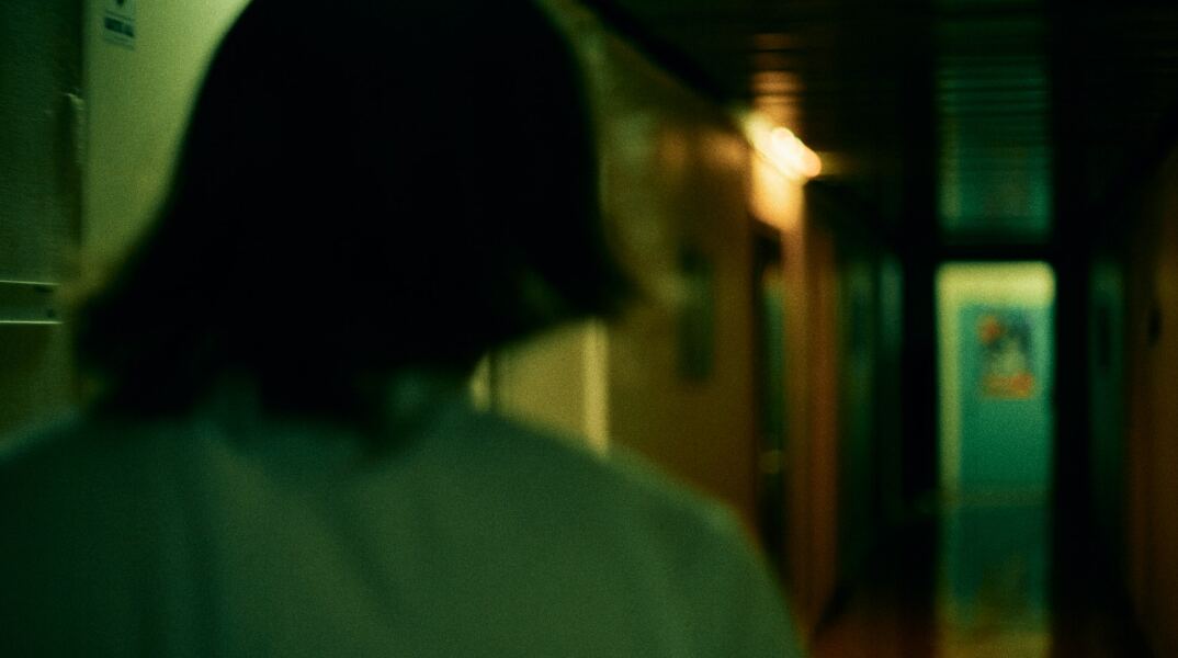 Γυναίκα γυρισμένη πλάτη σε σκοτεινό διάδρομο - Εικόνα που παραπέμπει σε κακοποίηση και μυστήριο