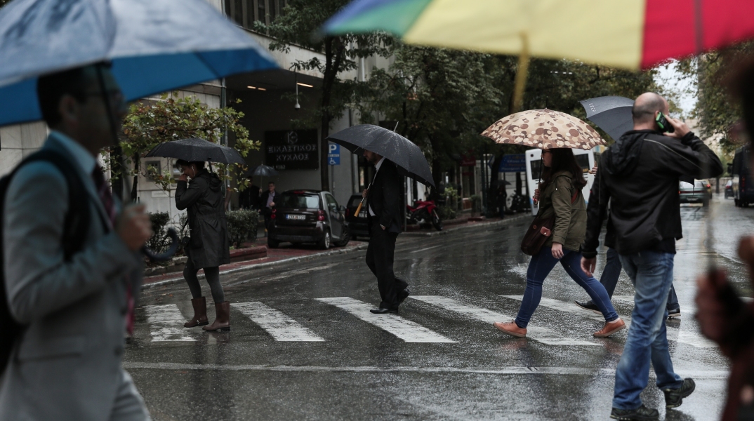 Πολίτες με ομπρέλες προστατεύονται από τη βροχή