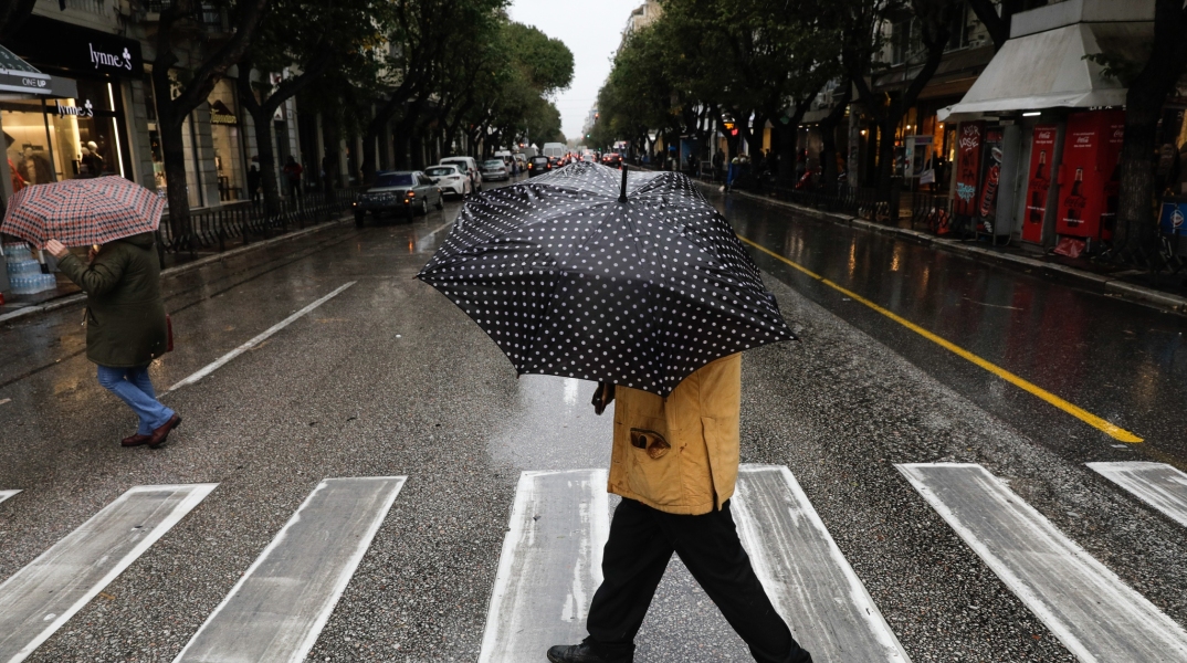 Πολίτες με ομπρέλα περνούν διάβαση στο κέντρο της Θεσσαλονικης