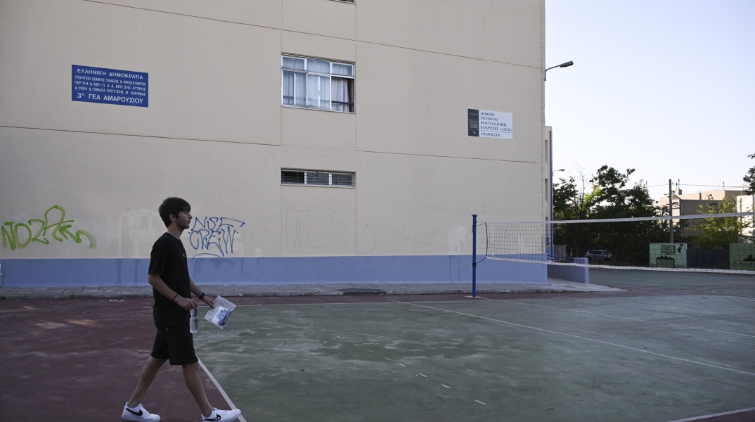 Μαθητής σε προαύλιο σχολείου με κάποια έγγραφα ανά χείρας