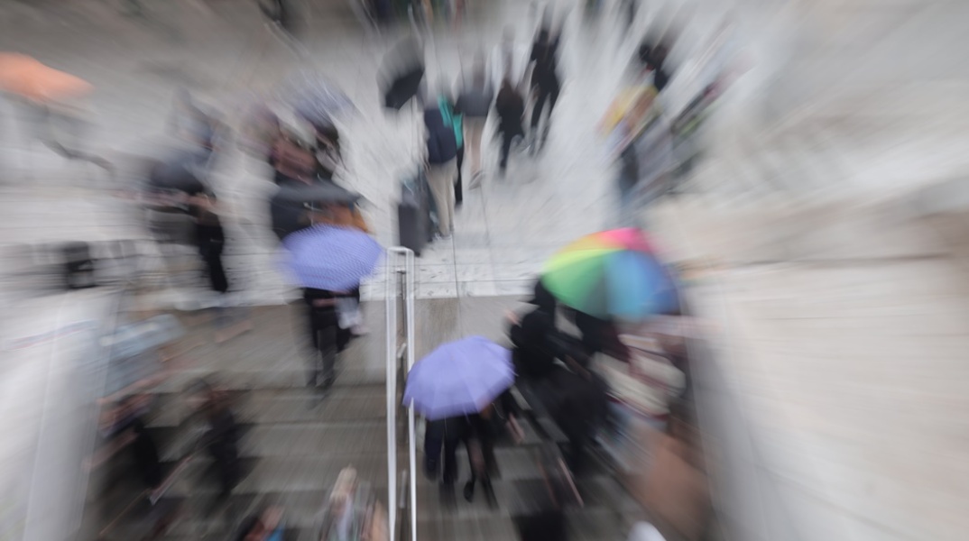 Πολίτες με ομπρέλα βγαίνουν από το μετρό Συντάγματος