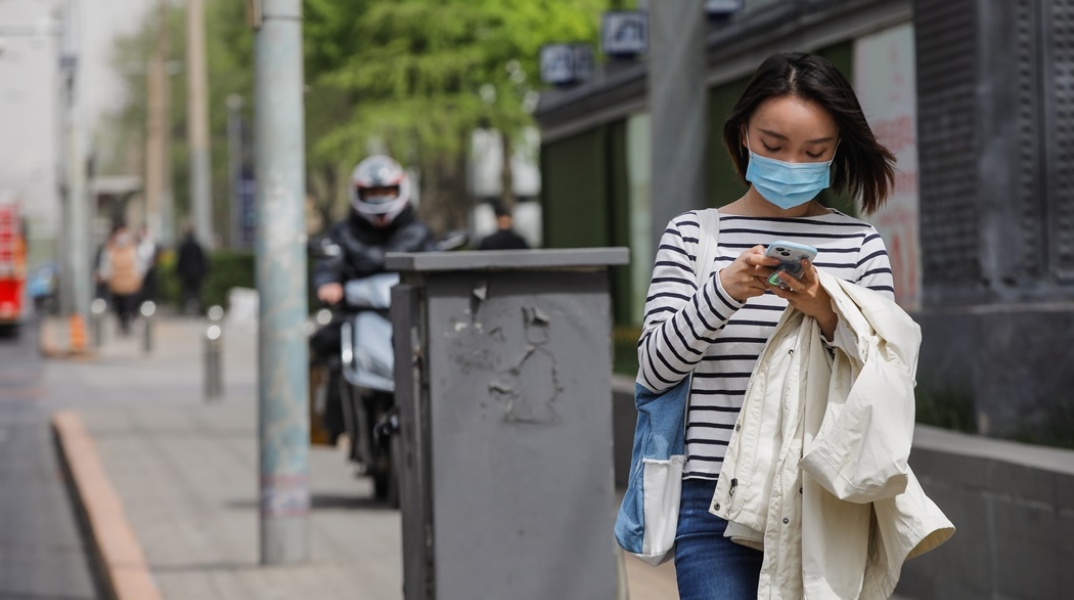 Γυναίκα με μάσκα προστασίας από τον κορωνοϊό περπατά σε δρόμο του Πεκίνου