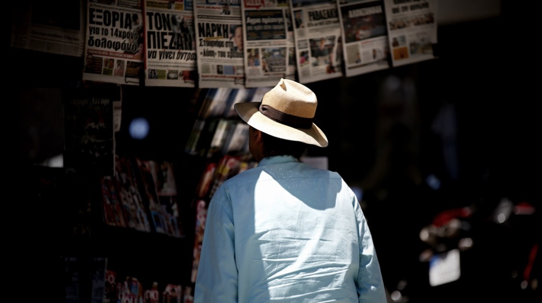 Εφημερίδες κρεμασμένες σε περίπτερο και άνδρας με καπέλο να διαβάζει τα πρωτοσέλιδα