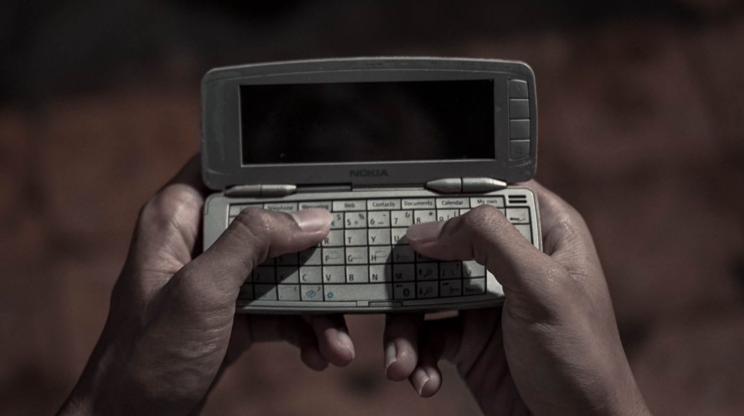 Γυναίκα κρατά στα χέρια της ένα παλιό κινητό και πληκτρολογεί