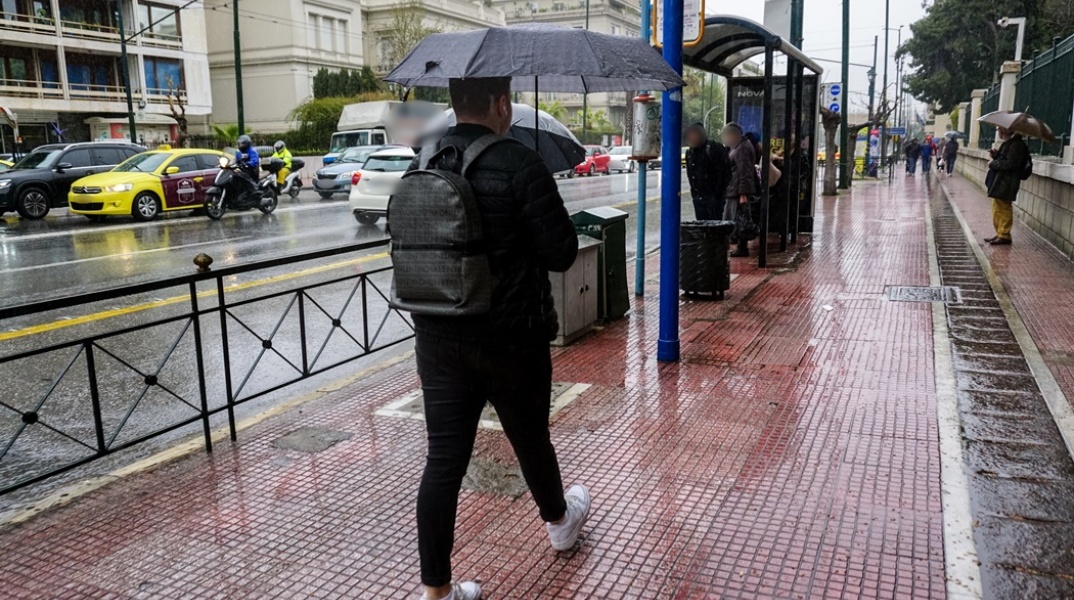 Νεαρός με ομπρέλα περπατά σε δρόμο της Αθήνας ενώ βρέχει