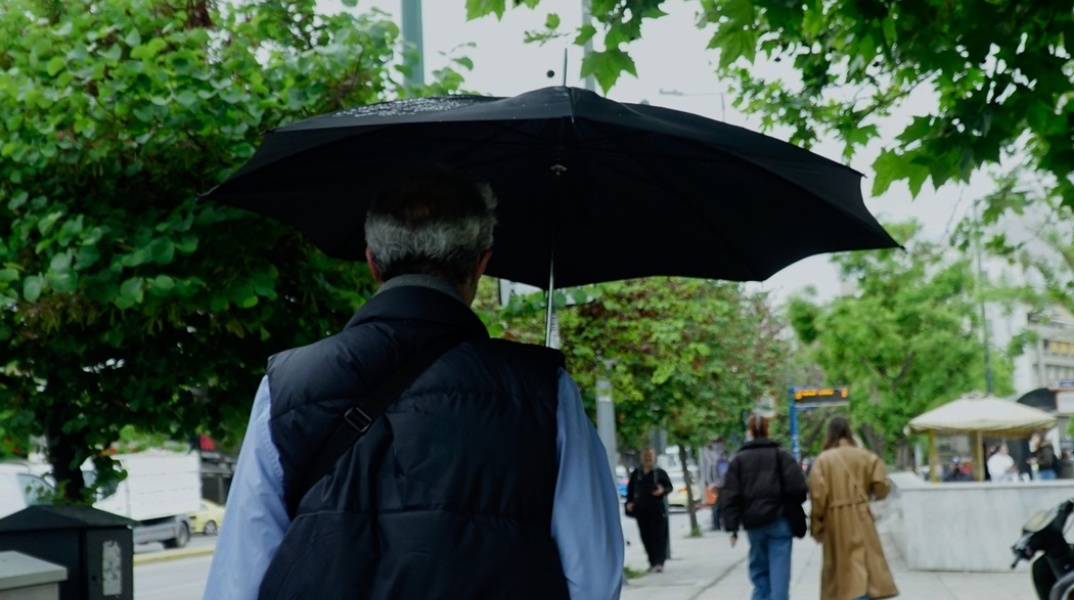 Άνδρας με ομπρέλα περπατά υπό βροχή