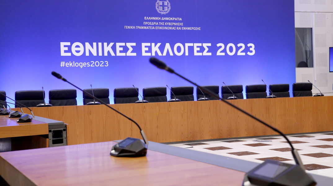 Στιγμιότυπο από το Κέντρο Τύπου στο Ζάππειο για τις εκλογές του 2023 - Δύο μικρόφωνα και πίσω οθόνη που γράφει «Εθνικές Εκλογές 2023» σε μπλε φόντο
