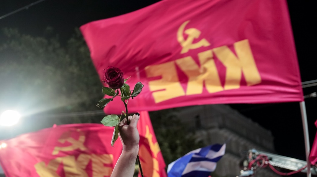 Σημαίες του ΚΚΕ και ένα χέρι που προτάσσει ένα κόκκινο λουλούδι