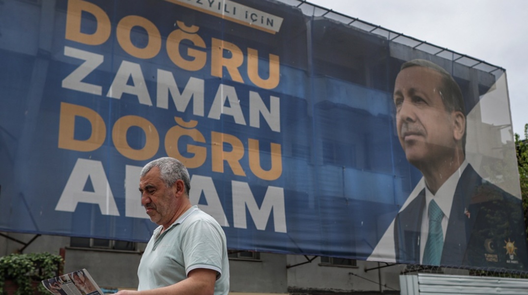 Προεκλογική αφίσα του Ρετζέπ Ταγίπ Ερντογάν σε δρόμο της Τουρκίας και πολίτης που περνά μπροστά από αυτή, κρατώντας την εφημερίδα του