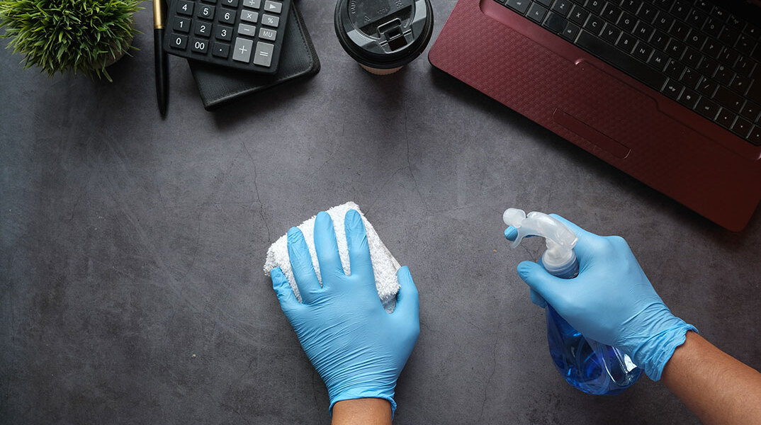 Χέρια με γάντια καθαρίζουν γραφείο