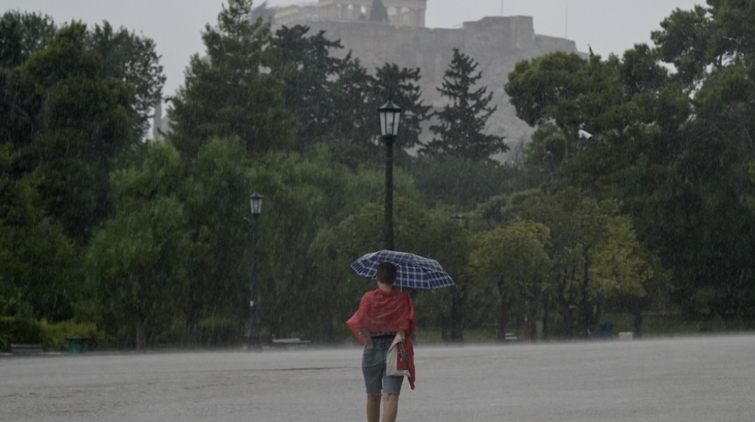 Γυναίκα με ομπρέλα περπατά σε δρόμο της Αθήνας