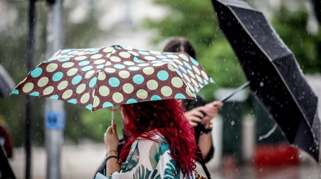 Γυναίκες με ομπρέλες προστατεύονται από καταιγίδα ενώ περπατούν στον δρόμο