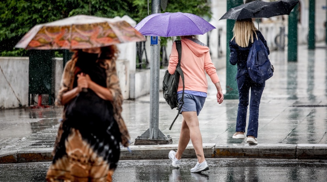 Γυναίκες με ομπρέλες στο κέντρο της Αθήνας προστατεύονται από αστάθεια του καιρού που εκδηλώνεται με καταιγίδες τις μεσημεριανές ώρες