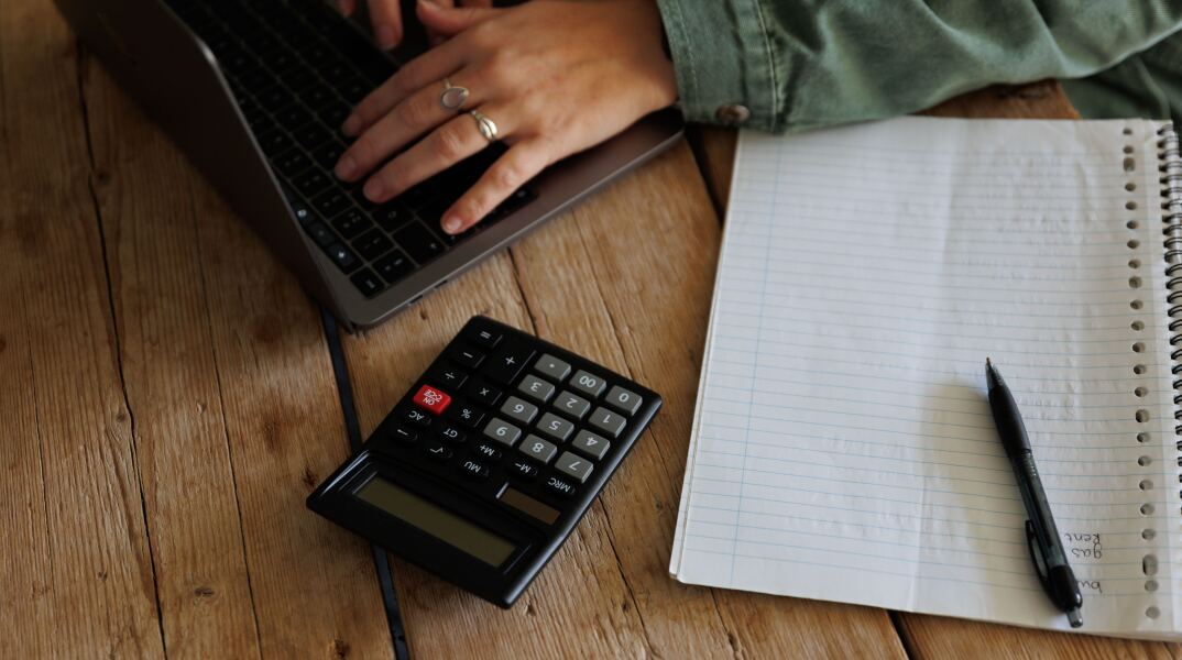 Άτομο υπολογίζει τα οικονομικά του σε κομπιουτεράκι, υπολογιστή και χαρτί
