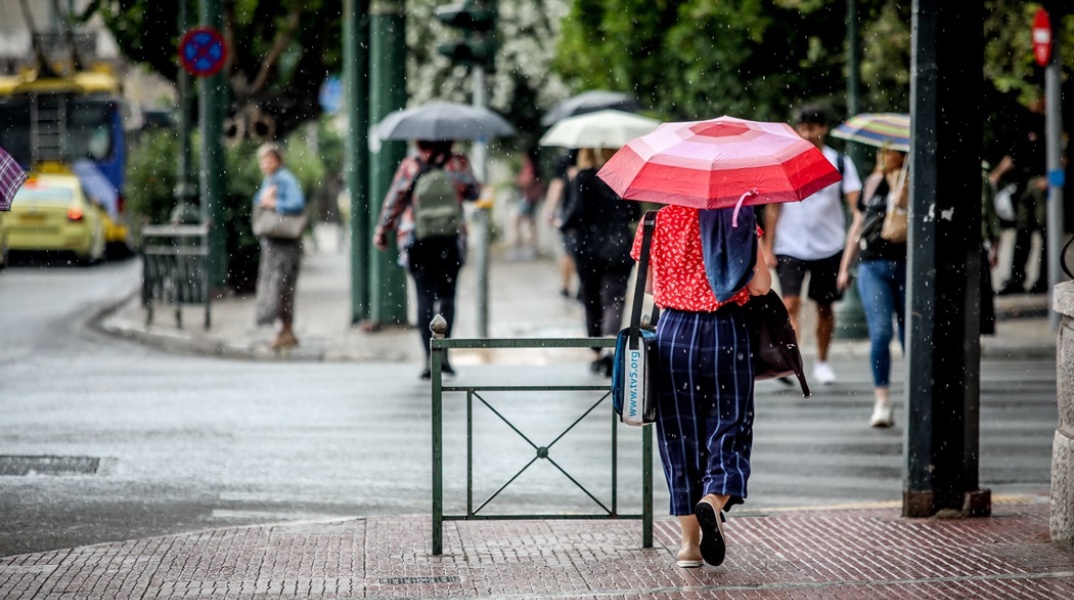 Πολίτες με ομπρέλες σε δρόμο της Αθήνας προστατεύονται από καλοκαιρινή βροχή