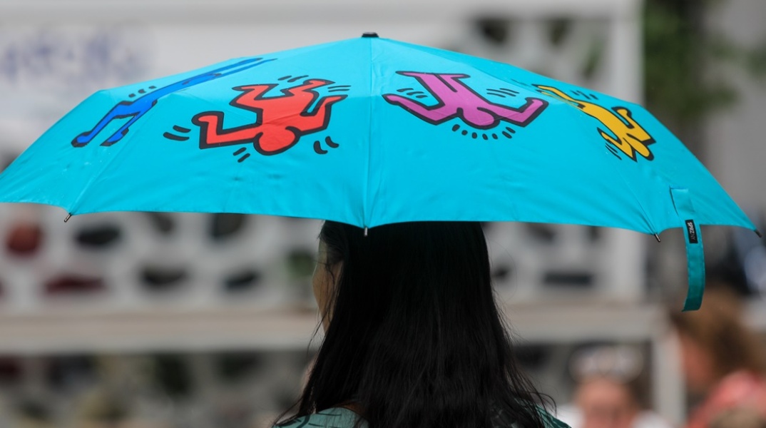 Γυναίκα με μπλε ομπρέλα προστατεύεται από τη βροχή