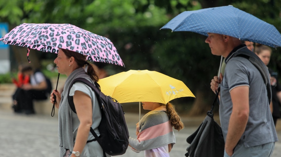 Γονείς και παιδί με μία ομπρέλα ο καθένας προστατεύονται από καλοκαιρινή βροχή στην Αθήνα
