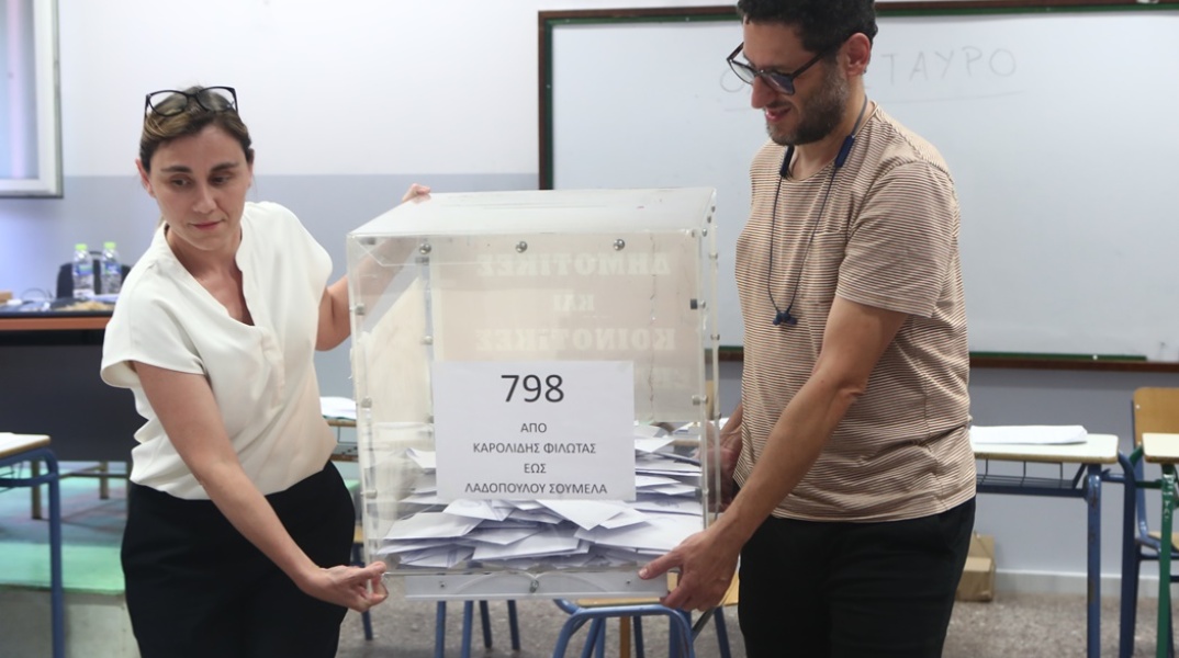 Δύο άτομα μεταφέρουν την κάλπη προκειμένου να την ανοίξουν και να καταγράψουν τις επιλογές των πολιτών