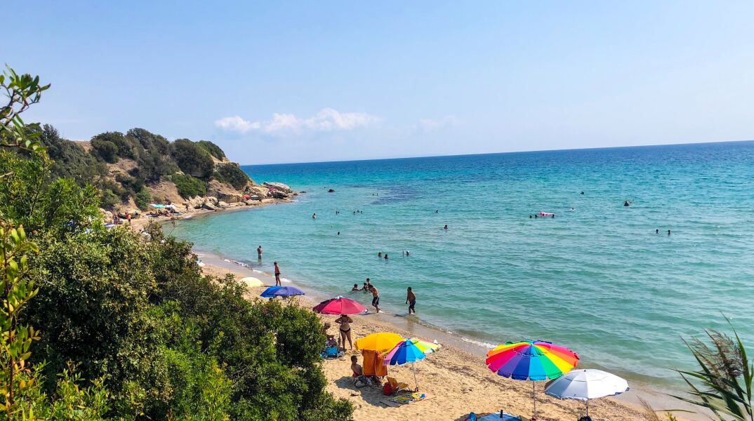 Πολίτες σε παραλία της Χαλκιδικής έχουν στήσει ομπρέλες και απλώσει ψάθες για να απολαύσουν τον ήλιο και τη θάλασσα