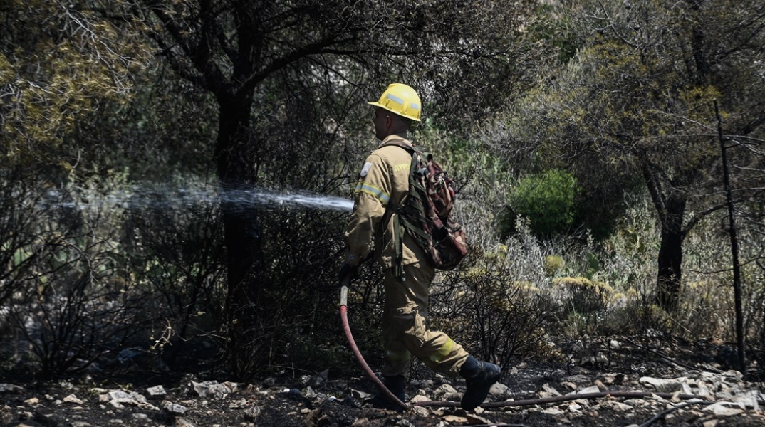 Πυροσβέστης με τη μάνικα ανά χείρας επιχειρεί για την κατάσβεσης φωτιάς