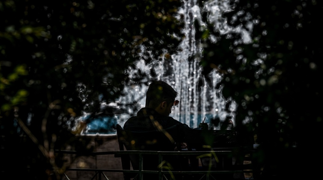 Πολίτης κάθεται σε καφέ κοντά σε σιντριβάνι και υπό τον ίσκιο φυτών