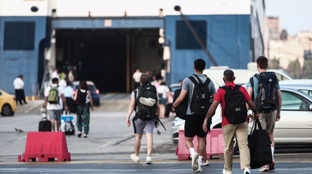 Ταξιδιώτες με τις βαλίτσες τους ετοιμάζονται για επιβίβαση σε πλοίο στο λιμάνι του Πειραιά