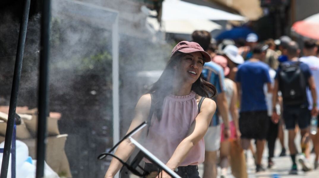 Κοπέλα περνά μπροστά από ανεμιστήρα που ψεκάζει νερό