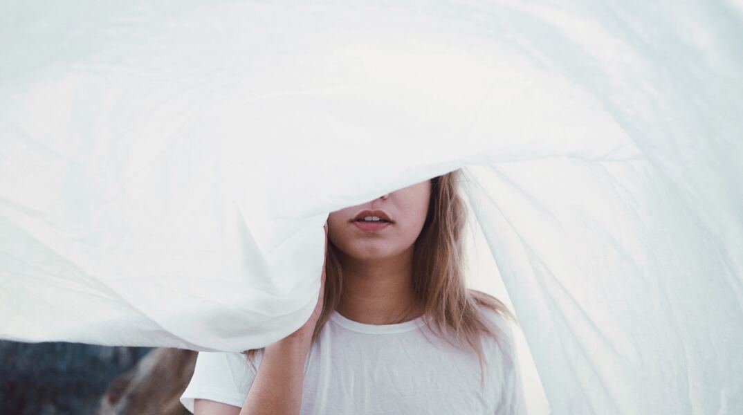 Νεαρή κοπέλα με κρυμμένο το πρόσωπό της από λευκό σεντόνι