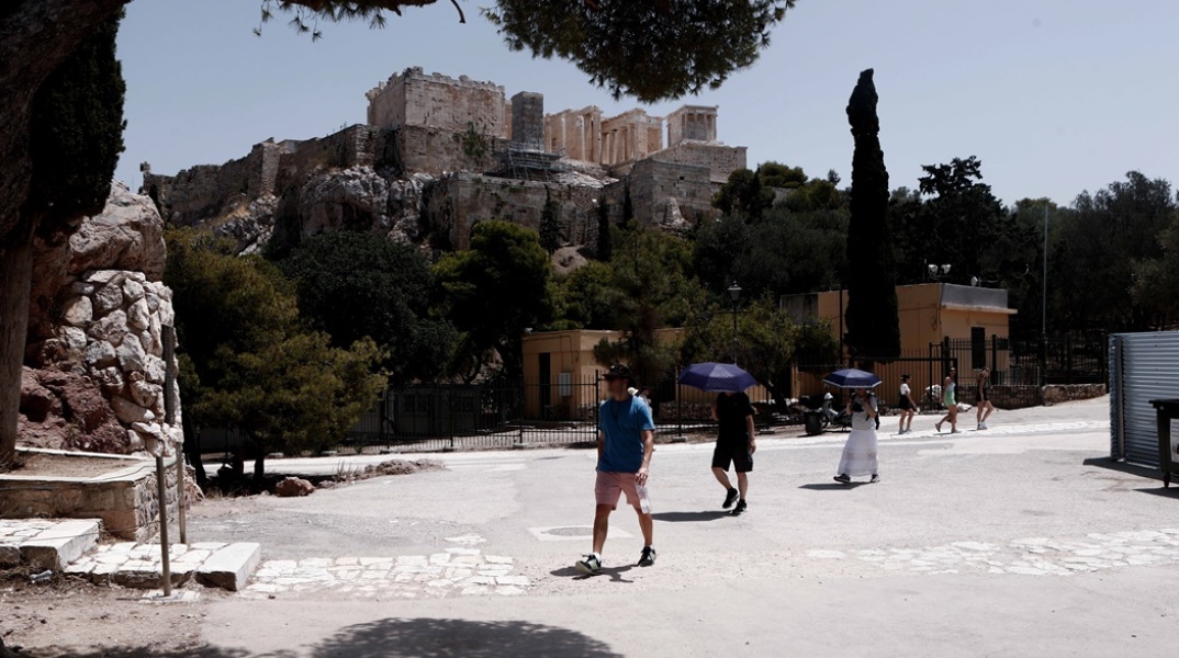 Πολίτες με ομπρέλες και καπέλα προστατεύονται από την ηλιακή ακτινοβολία