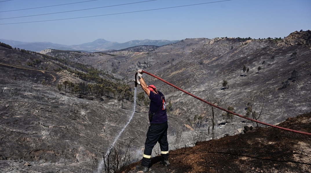 Πυροσβέστης επιχειρεί με μάνικα σε σημείο όπου η φωτιά σβήνει 