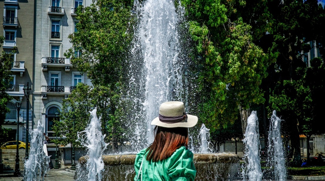 Γυναίκα με καπέλο μπροστά από το σιντριβάνι στην πλατεία Συντάγματος